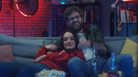 Young-Happy-Boyfriend-And-Girlfriend-Resting-On-The-Sofa-At-Night,-Smiling-And-Watching-Movie-On-Tv