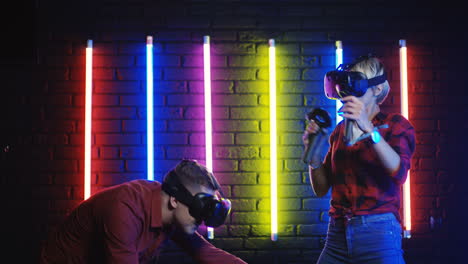 Fröhlicher-Freund-Und-Freundin-In-Vr-Brille,-Die-Ein-Virtual-Reality-Spiel-Spielen-Und-Mit-Joysticks-Mit-Neonfarbener-Wand-Im-Hintergrund-Schießen