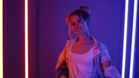 Young-Blond-Stylish-Girl-Dacing-Looking-At-Camera-On-Pink-And-Violet-Neon-Light-Background