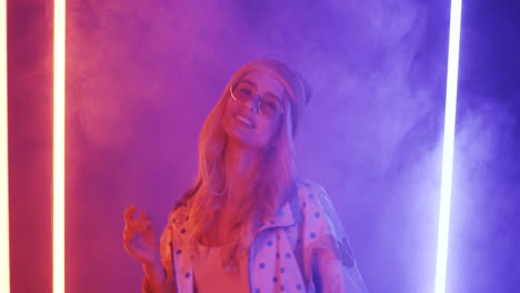 Cheerful-Stylish-Blonde-Girl-In-Hat-And-Sunglasses-Dancing-And-Smiling-With-The-Smoke-And-Neon-Lights