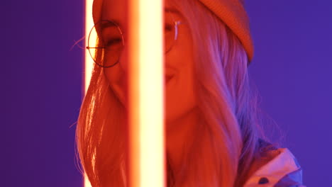 Close-Up-Of-Young-Blond-Beautiful-Woman-In-Hat-And-Glasses-Smiling-To-The-Camera-With-Neon-Lamps-Lights