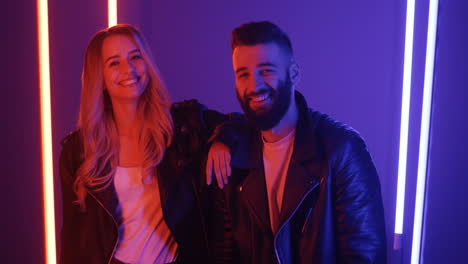Happy-Young-Man-And-Woman-Looking-At-Each-Other-And-Smiling-To-The-Camera-On-Purple-Neon-Lights-Background