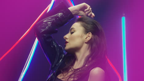 Close-Up-View-Of-Brunette-Woman-Dancing-Looking-At-Camera-In-Futuristic-Room-With-Neon-Lamps