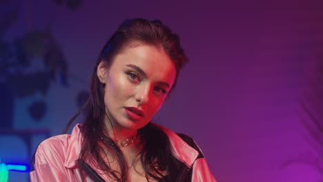 Close-Up-Of-Young-Woman-Looking-At-Camera-In-Room-With-Neon-Pink-And-Blue-Lights