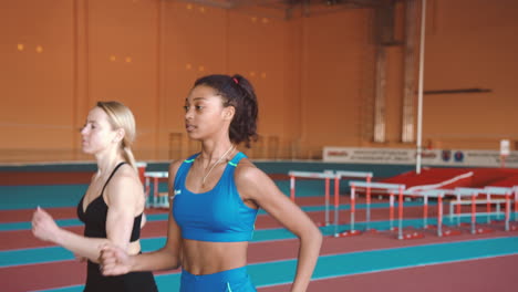 Two-Multiethnic-Female-Athletes-Running-Together-On-An-Indoor-Track-5
