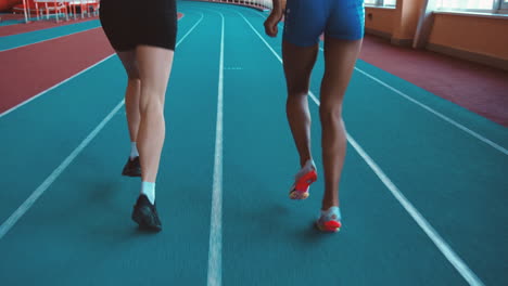 Rückansicht-Von-Zwei-Multiethnischen-Sportlerinnen,-Die-Zusammen-Auf-Einer-Indoor-Bahn-Laufen-1