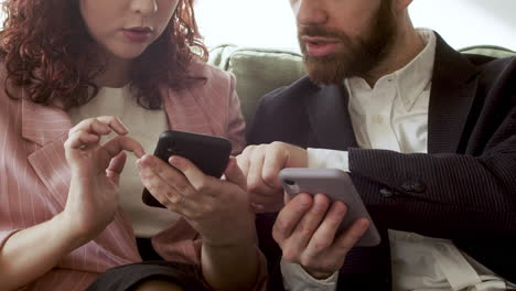 Close-Up-Of-Woman-And-Man-In-Formal-Wear-Using-Mobile-Phone-And-Talking-Together-While-Sitting-On-Sofa