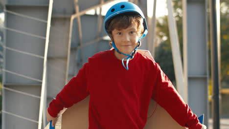 Cute-Little-Boy-In-Helmet-And-Red-Sweater-With-Cardboard-Airplane-Wings-Pretending-To-Fly