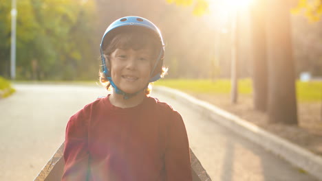 Portrait-Of-A-Cute-Little-Boy-In-Helmet-And-Red-Sweater-Looking-At-The-Camera-While-Standing-In-The-Park-On-A-Sunny-Day