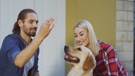 Close-Up-View-Of-Man-Sitting-With-Her-Girlfriend-Outdoors-And-Training-His-Labrador-Dog-To-Give-Five