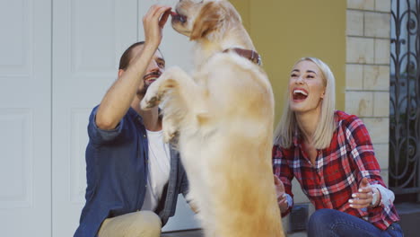 Close-Up-View-Of-Man-Sitting-With-Her-Girlfriend-Outdoors-And-Training-His-Labrador-Dog