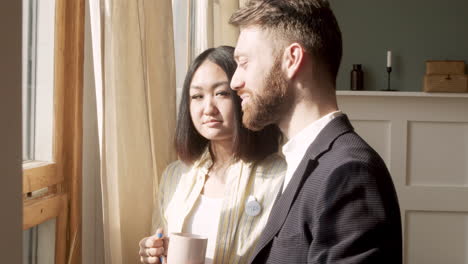 Bearded-Man-Talking-To-An-Woman-While-Standing-Near-The-Window-In-The-Morning