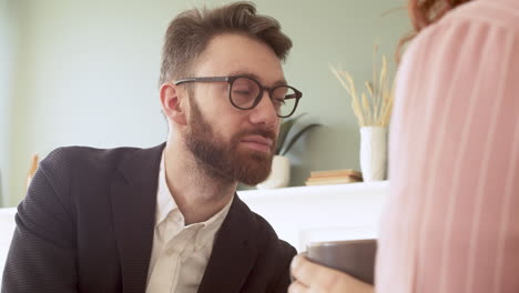 Close-Up-Of-A-Young-Man-With-Beard-And-Eyeglasses-Listening-Someone-Talking-While-Sitting-In-A-Modern-Living-Room