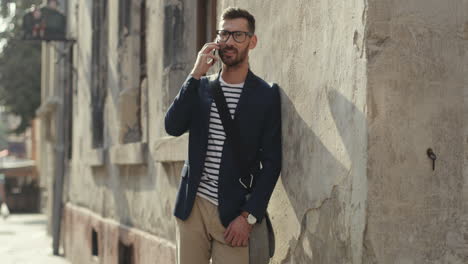 Stylish-Man-Leaning-Against-The-Wall-In-The-Old-Town-Street-And-Talking-On-The-Mobile-Phone