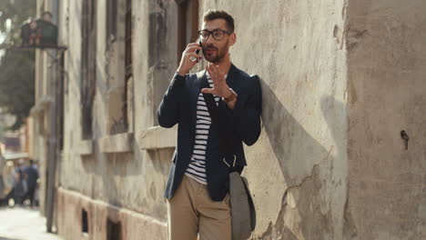 Happy-Stylish-Man-Leaning-Against-The-Wall-In-The-Old-Town-Street-And-Talking-On-The-Mobile-Phone