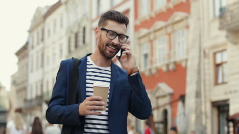 Handsome-Businessman-Holding-A-Takeaway-Coffee-Cup-And-Talking-On-The-Mobile-Phone-While-Walking-In-The-Street
