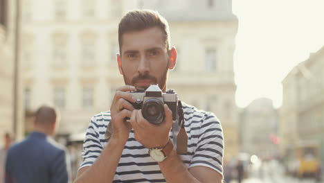 Portrait-Of-A-Handsome-Male-Photographer-Standing-In-The-Old-Town,-Taking-Photo-And-Then-Smiling-At-The-Camera