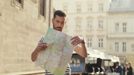 Lost-Male-Tourist-Holding-A-City-Map-And-Looking-For-Directions-In-The-Old-Town-Street