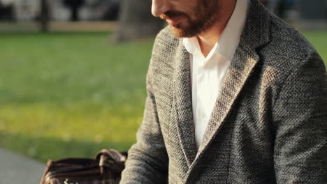 Close-Up-Of-A-Handsome-Businessman-Sitting-On-Wall-In-The-City-Park-And-Working-On-His-Laptop-Computer