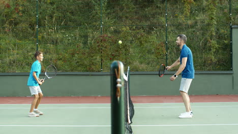 Side-View-Of-Happy-Father-And-Teen-Son-Playing-Tennis-On-Summer-Sunny-Day