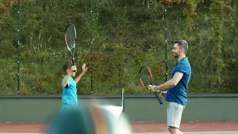 Side-View-Of-Dad-And-Teen-Son-Laughing-And-Cheering-Before-Or-After-Tennis-Game-Outdoors-At-Sport-Court