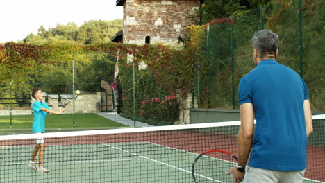 Rückansicht-Eines-Mannes,-Der-An-Einem-Sonnigen-Sommertag-Mit-Seinem-Jugendlichen-Sohn-Tennis-Spielt