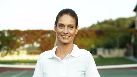 Portrait-Of-A-Beautiful-Woman-Standing-On-A-Tennis-Court-Holding-Racket-And-Smiling-Joyfully-At-The-Camera-1