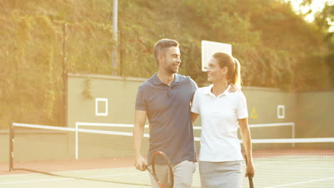 Glückliches-Paar,-Das-Den-Tennisplatz-Im-Sonnenlicht-Des-Sonnenuntergangs-Umarmt-Und-Verlässt-1