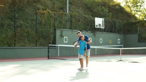 Man-Teaching-His-Teen-Son-How-To-Play-Tennis-On-A-Summer-Day