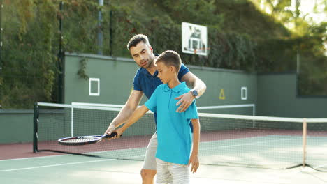 Mann-Bringt-Seinem-Jugendlichen-Sohn-An-Einem-Sommertag-Das-Tennisspielen-Bei-1
