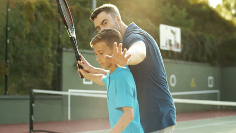 Man-Teaching-His-Teen-Son-How-To-Play-Tennis-On-A-Summer-Day-2