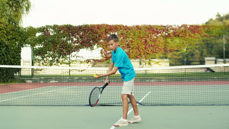 Teenager-Junge-Wirft-Ball-Auf-Den-Boden-Und-Schlägt-Dann-Mit-Schläger-Während-Des-Trainings-Auf-Dem-Tennisplatz-Im-Freien-An-Einem-Sommertag