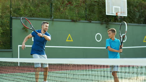 Mann-Bringt-Seinem-Jugendlichen-Sohn-Bei,-Wie-Man-Im-Sommer-Auf-Einem-Außenplatz-Tennis-Spielt