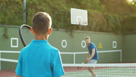 Rückansicht-Eines-Teenagers,-Der-Im-Sommer-Mit-Vater-Und-Kleiner-Schwester-Auf-Einem-Außenplatz-Tennis-Spielt