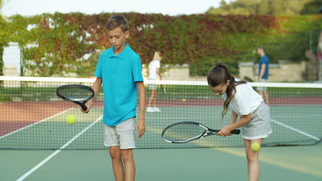 Sister-And-Brother-Playing-At-Tennis-Court-And-Hitting-Balls-Against-The-Ground-With-Racket