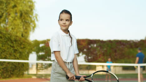 Porträtaufnahme-Eines-Hübschen-Mädchens-Im-Weißen-Poloshirt,-Das-Draußen-Auf-Dem-Tennisplatz-Steht-Und-Schläger-Hält
