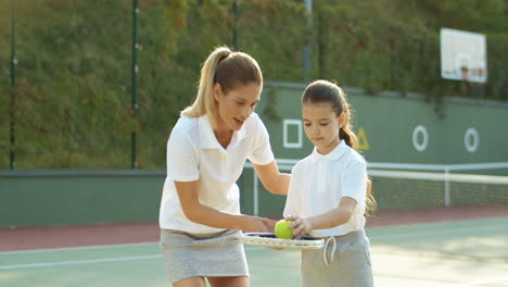 Woman-Teaching-Her-Daughter-How-To-Hit-Ball-With-Tennis-Racket-On-Sunny-Summer-Day