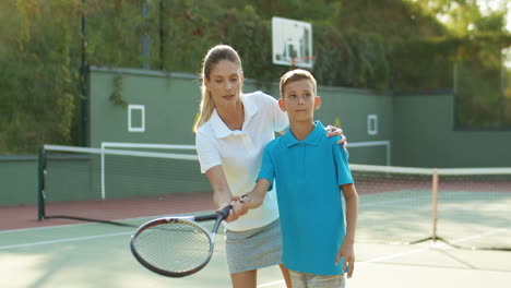 Woman-Teaching-Her-Son-How-To-Hit-Ball-With-Tennis-Racket-On-Sunny-Summer-Day