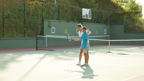 Woman-Teaching-His-Teen-Son-How-To-Play-Tennis-On-A-Summer-Day-1