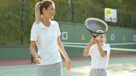 Woman-Teaching-Her-Little-Daughter-How-To-Hit-Ball-With-Racket-At-Tennis-Court-On-Sunny-Summer-Day
