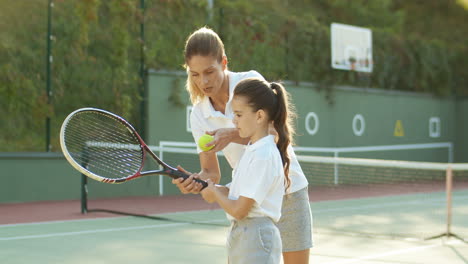 Loving-Woman-Teaching-Her-Cute-Little-Daughter-How-To-Play-Tennis-At-Sport-Court-On-A-Summer-Day-1