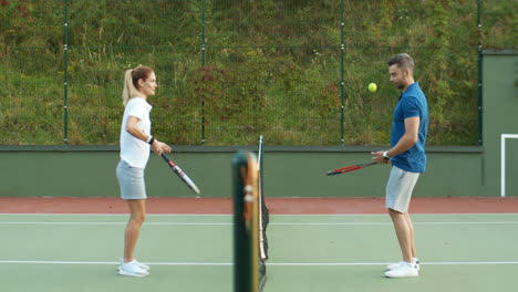 Side-View-Of-A-Happy-Couple-Playing-Tennis-At-Outdoor-Court-On-A-Summer-Day