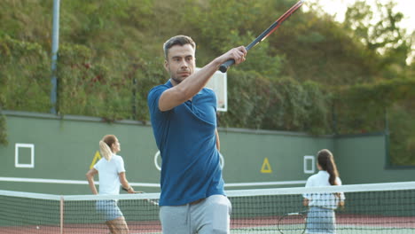 Handsome-Man-Training-And-Hitting-Ball-With-Racket-While-His-Family-Playing-Tennis-In-The-Background-1