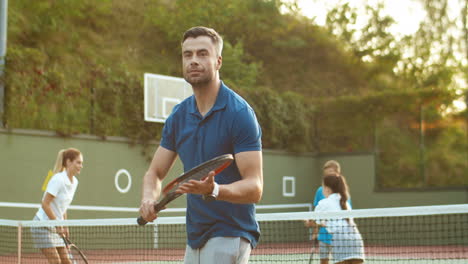 Schöner-Mann-Trainiert-Mit-Schläger,-Während-Seine-Familie-Im-Hintergrund-Tennis-Spielt