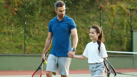 Liebevoller-Vater-Und-Süße-Kleine-Tochter,-Die-Händchen-Halten-Und-Gemeinsam-Den-Tennisplatz-Verlassen