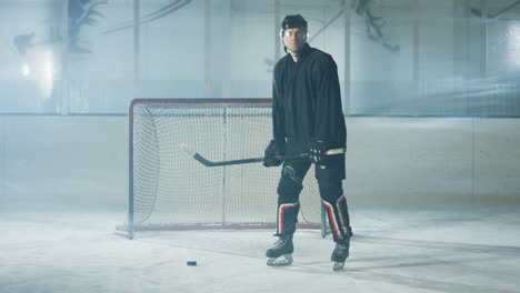 Porträt-Eines-Konzentrierten-Männlichen-Hockeyspielers-In-Uniform-Und-Helm,-Der-Mit-Schläger-Und-Puck-Auf-Der-Eisarena-Steht,-Während-Er-In-Die-Kamera-Blickt