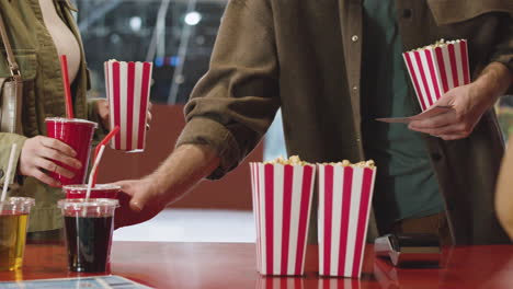Close-Up-Of-An-Unrecognizable-Couple-Buying-Movie-Tickets,-Popcorn-And-Soft-Drinks-At-Cinema-Counter