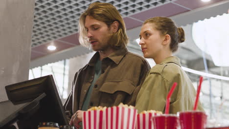 Happy-Couple-Selecting-Movie-From-Screen-And-Buying-Tickets-At-Cinema-1