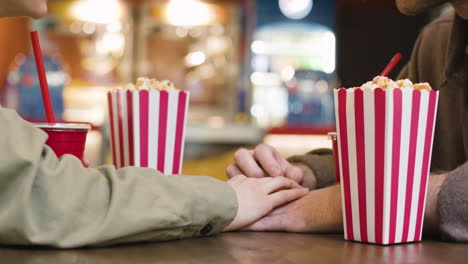 Loving-Couple-Holding-Hands-While-Sitting-At-Table-In-The-Cinema-Snack-Bar-1