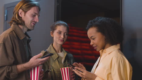 Glückliches-Paar-Mit-Popcorn-box,-Die-Dem-Weiblichen-Kinoplatzanweiser-Eine-Qr-kinokarte-Auf-Einem-Handy-Zeigt